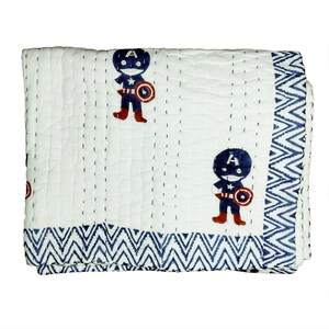 May include: White quilted blanket with a repeating pattern of a cartoon superhero in a blue and red costume. The blanket has a blue zigzag border and is stitched with dark blue thread.