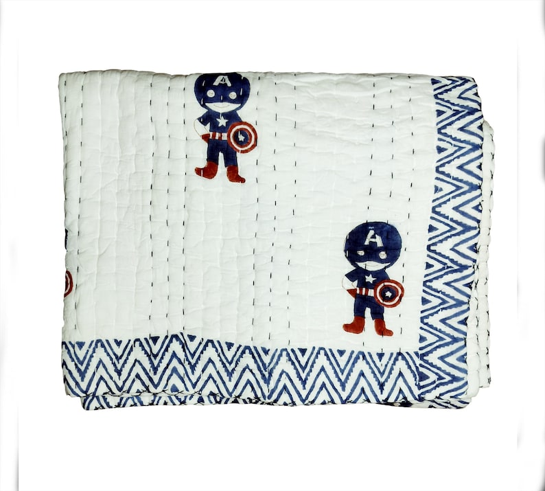 May include: White quilted blanket with a repeating pattern of a cartoon superhero in a blue and red costume. The blanket has a blue zigzag border and is stitched with dark blue thread.