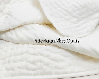 Könnte beinhalten: Weiße gesteppte Decke mit subtiler Textur. Die Decke ist in der Mitte gefaltet und die Kanten sind sichtbar. Der Text "Pitter Rugs Nbed Quilts" ist in der Mitte des Bildes sichtbar.