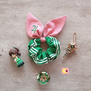 May include: A selection of accessories including a green and white scrunchie with pink bunny ears, a gold star wand, a green compact, a figurine, and a pink logo with a crescent moon and bunny.