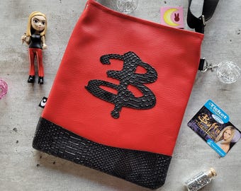 May include: Red and black faux leather shoulder bag with a black leather 'B' symbol. The bag has a black adjustable strap and a silver chain.