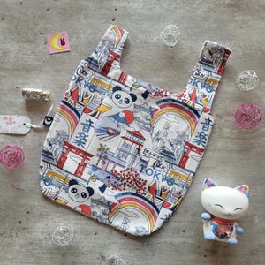 Puede incluir: Una bolsa de tela reutilizable blanca con un diseño de inspiración japonesa. La bolsa presenta un panda, flores de cerezo, una puerta torii roja y el texto "音楽" y "TOKYO".