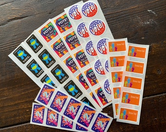 May include: Sticker sheets with "VOTE" printed on them, alongside other text and graphics. Some stickers say "Your Voice Matters!" and "Heroes Vote!". The stickers are on a wooden surface.