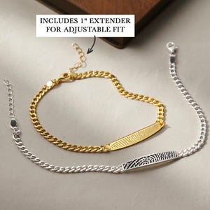 Könnte beinhalten: Zwei Fingerabdruck-ID-Armbänder. Eines ist goldfarben, das andere silberfarben. Beide haben ein Panzerketten-Design und eine Verlängerung für eine verstellbare Passform. Das goldene Armband hat einen Fingerabdruck auf der ID-Leiste.