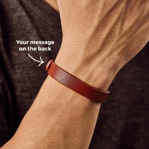 May include: A brown leather bracelet with a silver buckle. The bracelet is worn on a person's wrist. The text "Your message on the back" is written on the image.