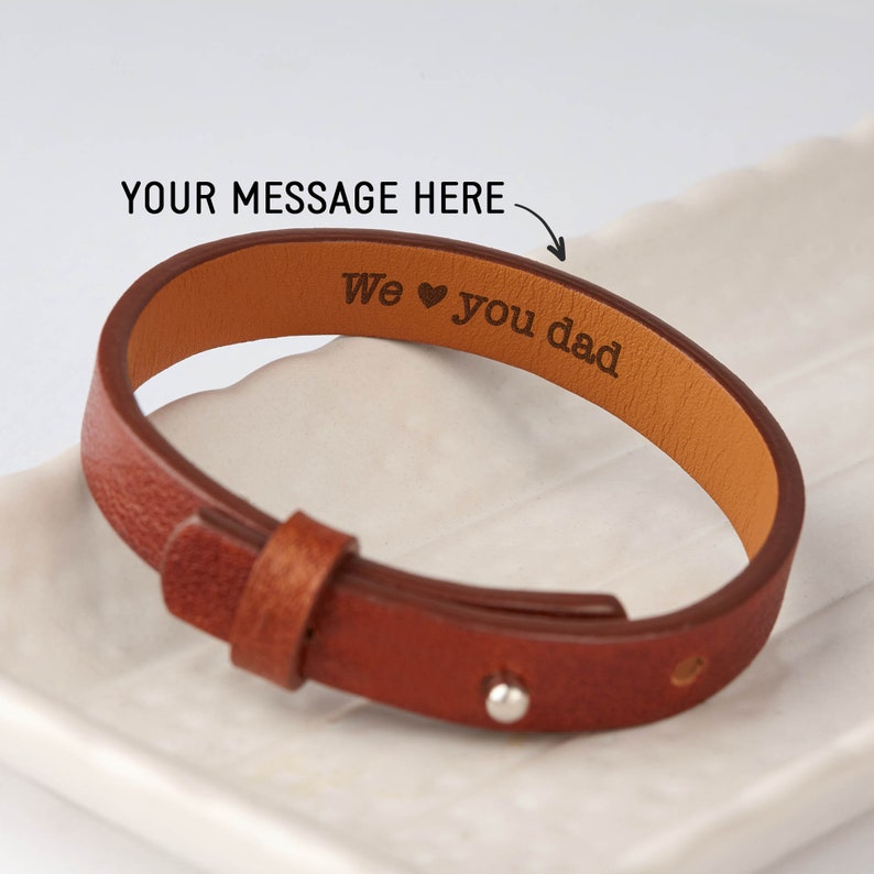 May include: Brown leather bracelet with a silver clasp. The bracelet is engraved with the text "We &hearts; you dad".