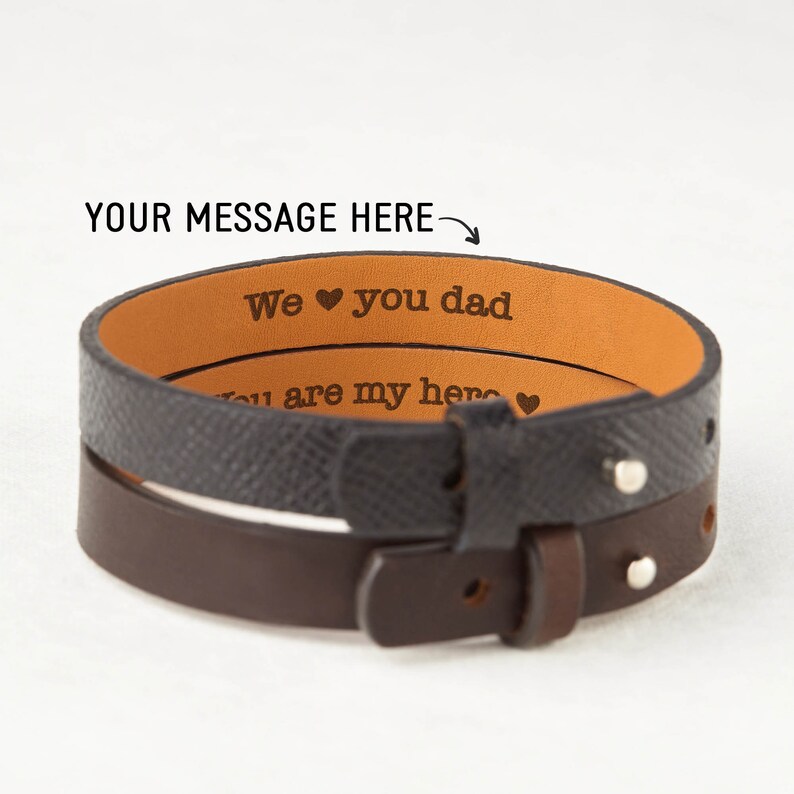 May include: A brown and black leather wrap bracelet with a personalized message that reads "We &hearts; you dad" and "You are my hero &hearts;".
