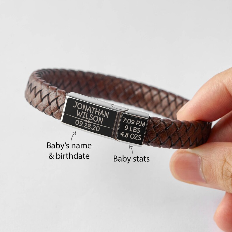 Puede incluir: Una pulsera trenzada de cuero marr&oacute;n con un cierre plateado. El cierre est&aacute; grabado con el nombre "JONATHAN WILSON" y la fecha "09.28.20". La pulsera tambi&eacute;n muestra las estad&iacute;sticas del beb&eacute;: 19:09, 4,08 kg y 136 g.
