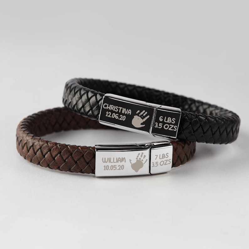 Puede incluir: Dos pulseras de cuero con placas de acero inoxidable grabadas. La pulsera superior es negra y la inferior es marr&oacute;n. Las placas tienen los nombres Christina y William, las fechas de nacimiento, las huellas de las manos y los pesos y las onzas.