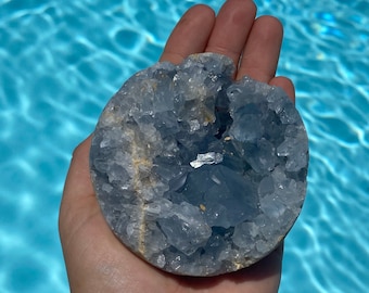 May include: A blue celestite crystal cluster with a rough, natural surface. The crystal is in the shape of a sphere and has a variety of sizes and shapes of crystals.