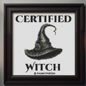 May include: A black framed print with white text that reads "CERTIFIED WITCH" and a black witch's hat with a green brim and a pointed top. The text "© PHUNKYPHRESH" is below the hat.