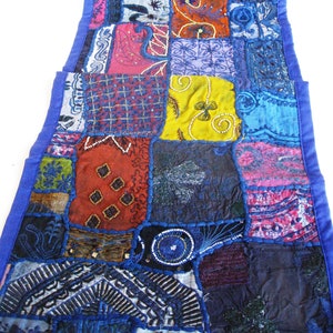 Peut inclure: Un long chemin de table rectangulaire en patchwork avec une bordure bleue. Le chemin de table est compos&eacute; de diff&eacute;rents tissus de couleurs et de motifs vari&eacute;s, notamment rouge, vert, jaune et violet. Le chemin de table est d&eacute;cor&eacute; de perles et de paillettes.