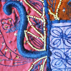 Peut inclure: Gros plan sur un patchwork de tissu color&eacute; avec des broderies bleues, rouges et blanches. Le tissu est d&eacute;cor&eacute; de perles et de paillettes.