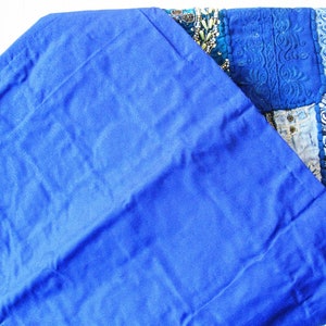 Peut inclure: Un tissu bleu roi avec un bord pli&eacute;. Le tissu est lisse et a un l&eacute;ger brillant. Le tissu est pli&eacute; sur une courtepointe patchwork color&eacute;e avec des broderies complexes et des embellissements perl&eacute;s.