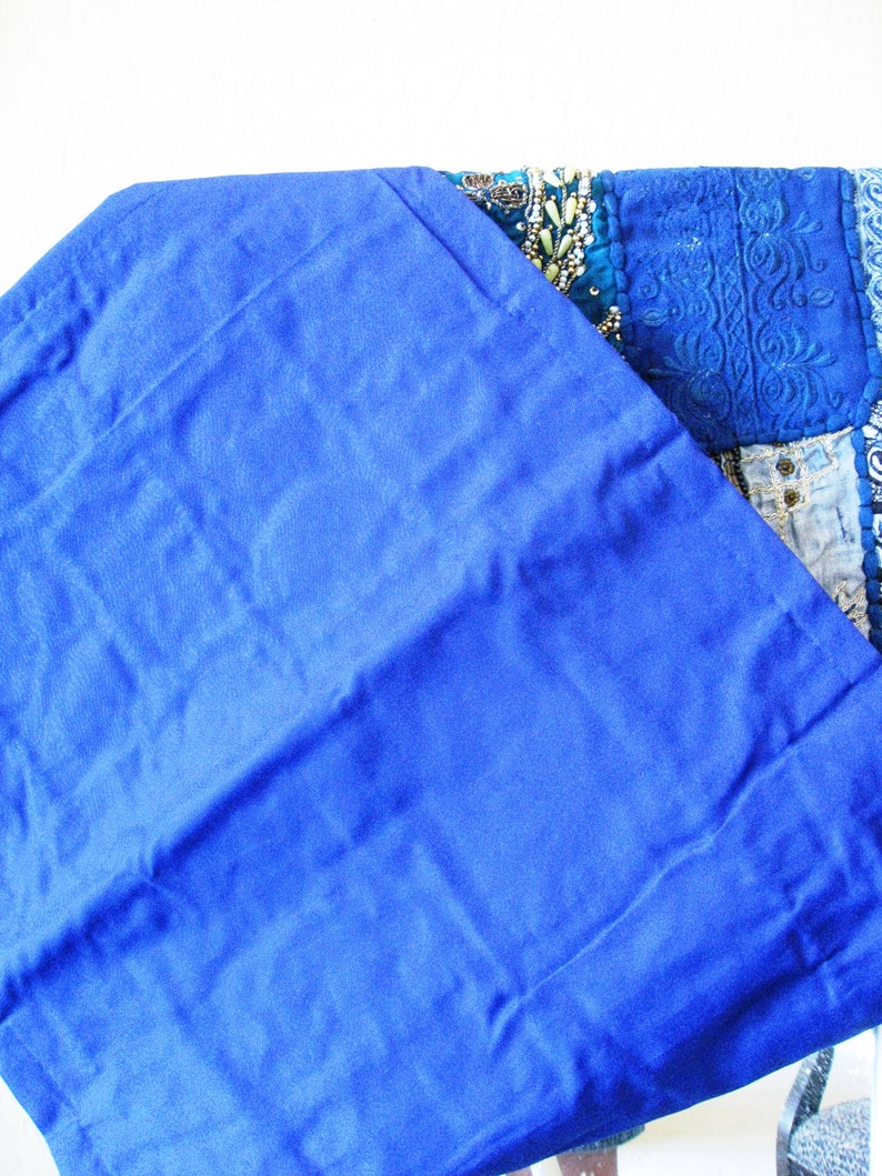 Peut inclure: Un tissu bleu roi avec un bord pli&eacute;. Le tissu est lisse et a un l&eacute;ger brillant. Le tissu est pli&eacute; sur une courtepointe patchwork color&eacute;e avec des broderies complexes et des embellissements perl&eacute;s.