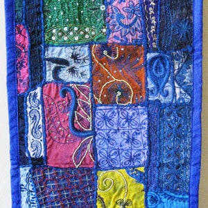 Peut inclure: Une courtepointe patchwork avec une bordure bleue et diff&eacute;rentes cases de tissu color&eacute;. La courtepointe pr&eacute;sente des broderies et des perles complexes, cr&eacute;ant un design unique et textur&eacute;.
