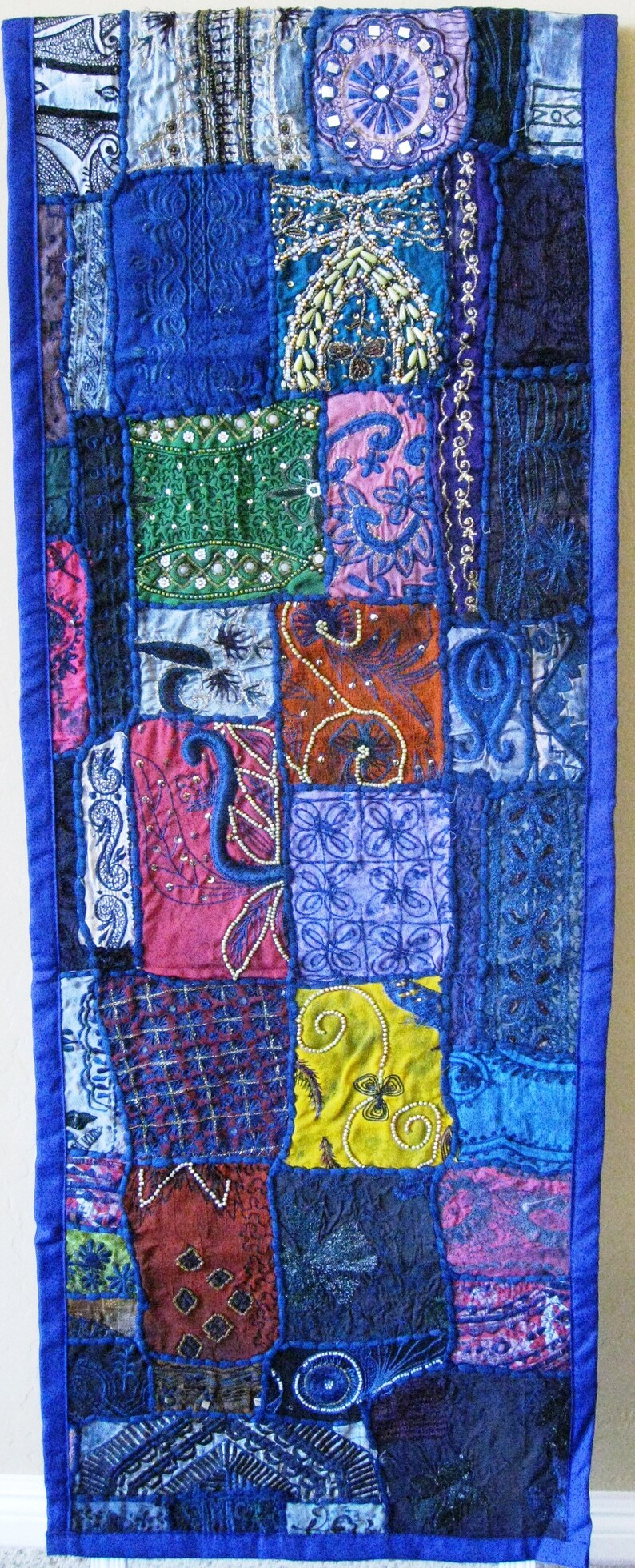 Peut inclure: Une courtepointe patchwork avec une bordure bleue et diff&eacute;rentes cases de tissu color&eacute;. La courtepointe pr&eacute;sente des broderies et des perles complexes, cr&eacute;ant un design unique et textur&eacute;.