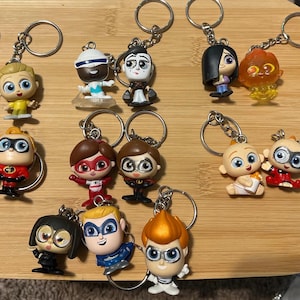 May include: A collection of 12 colorful keychains featuring characters from the animated film Incredibles 2. The keychains are made of plastic and feature characters such as Mr. Incredible, Elastigirl, Violet, Dash, Jack-Jack, and Syndrome.