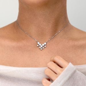 May include: A silver necklace with a pendant of small, round, white gemstones. The necklace is worn around the neck, with the gemstones positioned below the collarbone. The design is simple and elegant, suitable for everyday wear or special occasions.