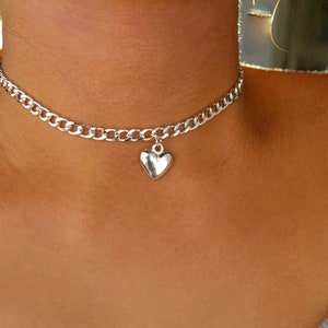 May include: A silver chain choker necklace with a silver heart pendant.