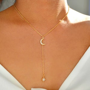 May include: A gold chain necklace with a crescent moon pendant and a star charm. The moon pendant is adorned with small clear crystals.