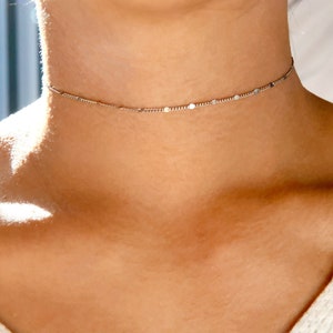 May include: A delicate silver chain choker necklace with small, evenly spaced round accents.