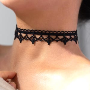 May include: Black lace choker necklace with a scalloped edge and diamond-shaped details. The delicate choker is worn around the neck. The jewelry is a fashion accessory.