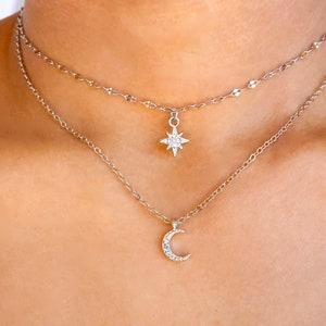 May include: A silver layered necklace with a crescent moon pendant and a star pendant, both adorned with small clear crystals.