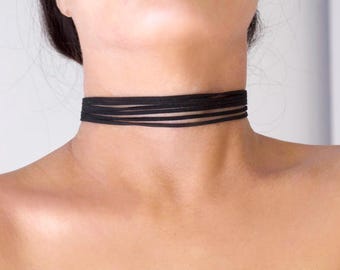 May include: A black choker necklace with multiple thin, layered bands. The choker sits around the neck, showcasing a minimalist and versatile design. The accessory is a dark, solid color.