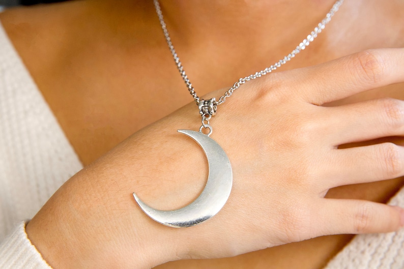 May include: A silver crescent moon pendant necklace. The pendant is large and hangs from a delicate silver chain.