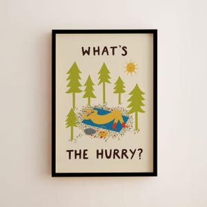 May include: A framed wall art print on a cream background featuring the text WHAT'S THE HURRY? in brown. The illustration shows a yellow figure resting on a blue blanket in a forest of green pine trees with a yellow sun and a small basket.