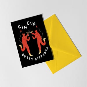 May include: A black greeting card with the words "CIN CIN" and "HAPPY BIRTHDAY" in white. The card features two red figures toasting with cocktails. A bright yellow envelope is next to the card.