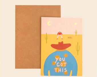 May include: A greeting card featuring a desert scene with a person in a blue shirt and red hat, with the text "YOU GOT THIS" surrounded by yellow sun icons. A smaller figure stands in the distance under a crescent moon. Includes a brown envelope.