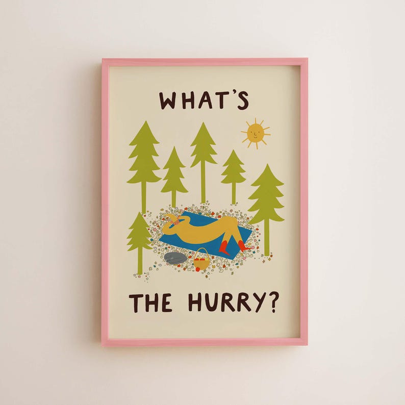 May include: A framed wall art print with a light cream background and a pink frame. The illustration features green pine trees, a yellow sun, and a figure resting on a blue blanket with red boots. The text reads WHAT'S THE HURRY? in brown.