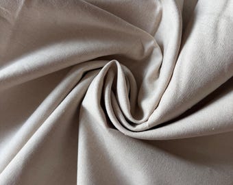 May include: A piece of off-white, unbleached cotton fabric featuring a dense, plain weave texture. The material is arranged in a swirling, gathered pattern that creates deep shadows and highlights across the surface of the textile.