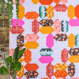 May include: A colorful quilt with a geometric pattern of octagons in shades of orange, pink, and brown. The quilt is hanging on a wooden wall.