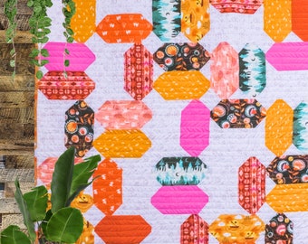May include: A colorful quilt with a geometric pattern of octagons in shades of orange, pink, and brown. The quilt is hanging on a wooden wall.