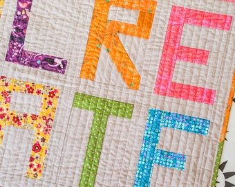 May include: A quilted wall hanging with the word "CREATE" spelled out in colorful fabric letters. Each letter is made from a different patterned fabric.