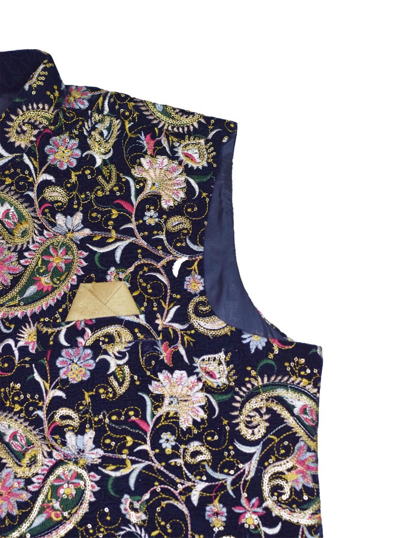 Op de afbeelding: Een marineblauwe vest met een ingewikkeld bloemen- en paisley patroon. Het ontwerp bevat gouden, roze en witte borduursels, met een klein gouden zakje. De vest heeft een satijnen voering en is een formeel kledingstuk.