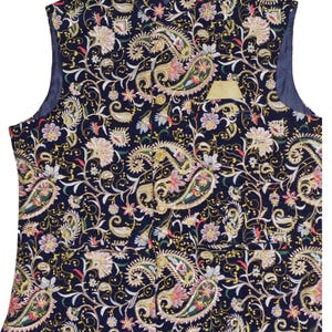 Op de afbeelding: Een marineblauwe vest met een paisley patroon in goud, roze en groen. De vest heeft een opstaande kraag en een kleine zak met een gouden rand. De mouwloze vest is volledig gevoerd.