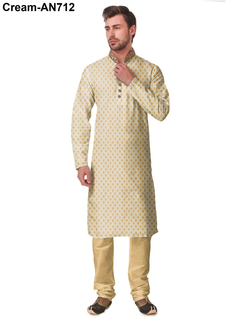 May include: Cream-colored kurta pajama set. The long-sleeved kurta features a gold diamond pattern and a mandarin collar with gold embroidery. The matching pajama pants are a solid cream color. The outfit is completed with black and gold embroidered shoes.