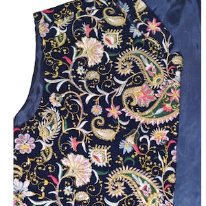 Op de afbeelding: Een marineblauwe vest met ingewikkelde bloemen- en paisley-borduurwerk in goud, roze en groen. Het ontwerp van de vest heeft gedetailleerde stiksels en een donkerblauwe voering, wat een klassieke, sierlijke stijl laat zien.