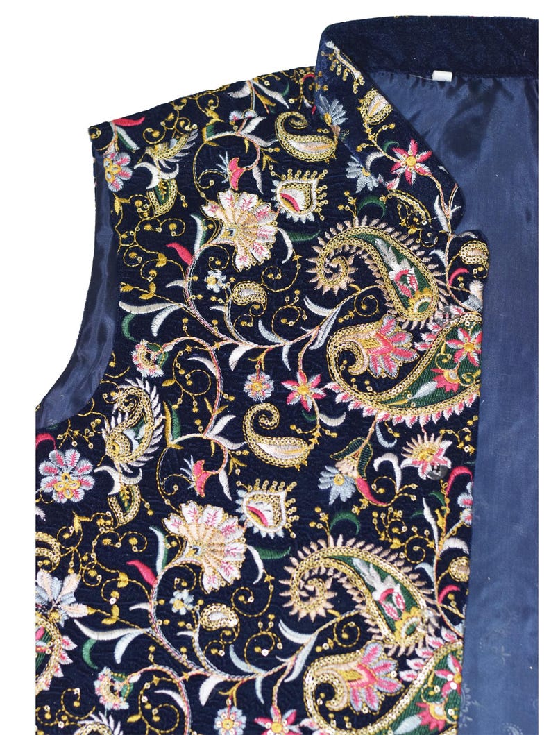 Op de afbeelding: Een marineblauwe vest met ingewikkelde bloemen- en paisley-borduurwerk in goud, roze en groen. Het ontwerp van de vest heeft gedetailleerde stiksels en een donkerblauwe voering, wat een klassieke, sierlijke stijl laat zien.