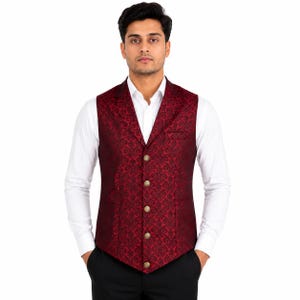 May include: A deep red waistcoat featuring a dark, intricate damask pattern, a V-neckline, and five metallic buttons down the front. The garment is worn over a crisp white long-sleeved button-down shirt and paired with solid black trousers.