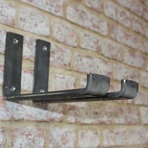 May include: A dark gray metal shelf with two vertical supports and a horizontal shelf, mounted on a brick wall. The shelf has a rustic, industrial design, with visible rivets. The brick wall is a mix of red, white, and tan bricks.