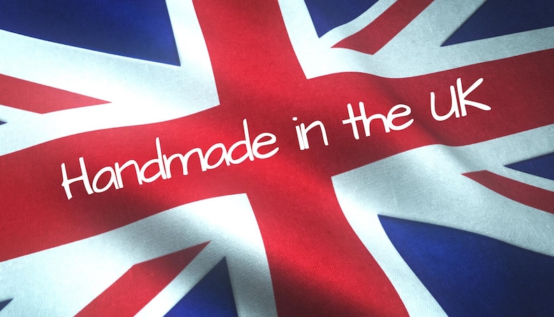May include: A fabric Union Jack flag featuring the red, white, and blue colors of the United Kingdom. The text "Handmade in the UK" is printed in a white, rounded, sans-serif font across the center of the flag, which has a wavy texture.
