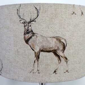 May include: A beige lampshade with a brown deer print. The deer is facing the left side of the image and has large antlers.