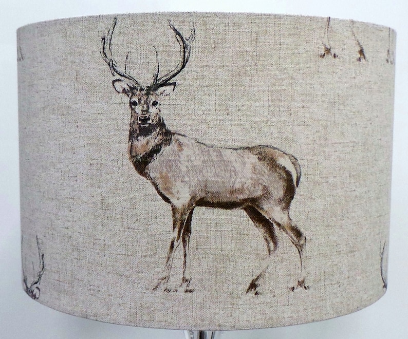 May include: A beige lampshade with a brown deer print. The deer is facing the left side of the image and has large antlers.