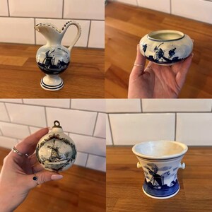 May include: A selection of Delftware pottery items, including a small jug, a round bowl, a Christmas bauble, and a small vase. Each piece is white with blue windmill and landscape designs. The jug has a handle and spout, the vase has two small handles.