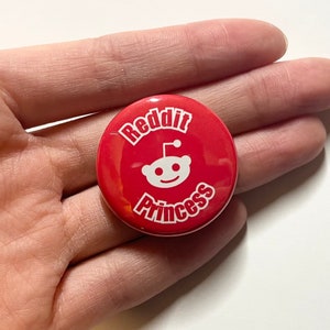 May include: A red button with the text "Reddit Princess" in white lettering. The Reddit alien logo is also in white.
